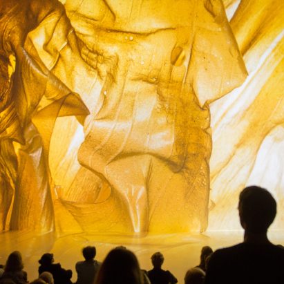 People viewing a projection of a flowing bronze fabric by a Fashion & Technology student