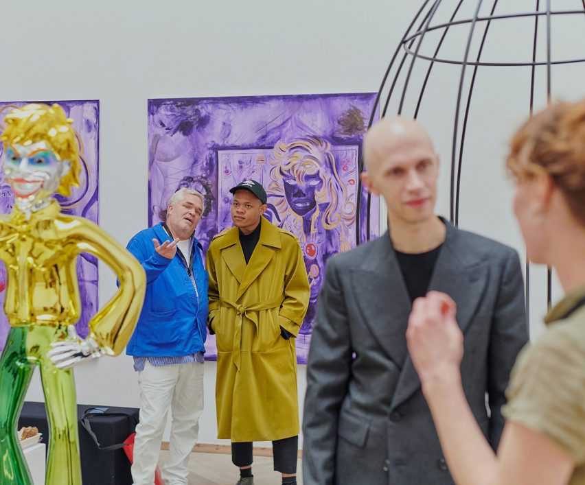 People looking at a yellow sculpture, a wired sculpture and a purple painting