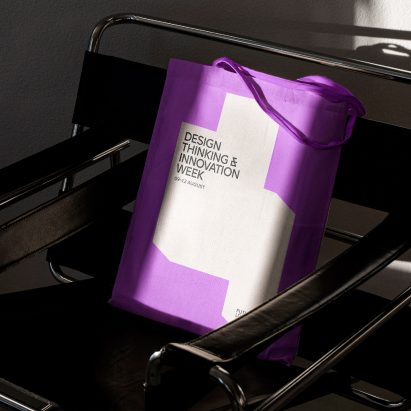 A photograph of a purple tote bag on a chair with the Design Thinking and Innovation Week logo