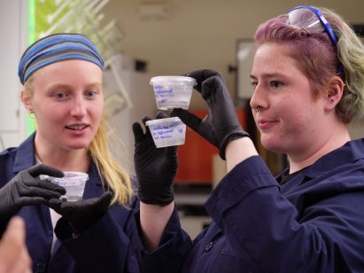 Researchers at the University of Colorado Boulder hold tubs of algae