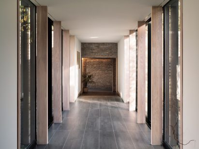 Long glass walkway lined with thin timber columns in home by Blee Halligan Architects