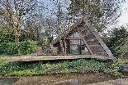 An angular cabin with terrace and seating in front of a stream
