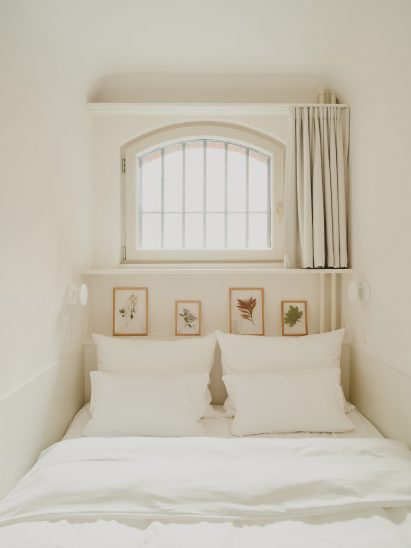 Narrow guest room with small window and white interior scheme by Grüntuch Ernst Architects