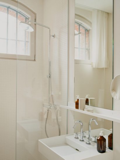 Bathroom in with small window and white tiles by Grüntuch Ernst Architects
