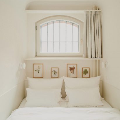 Narrow guest room with small window and white interior scheme by Grüntuch Ernst Architects