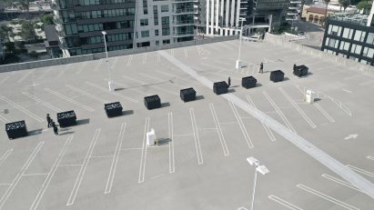 Black waste bins are lined in a row on top of a car park