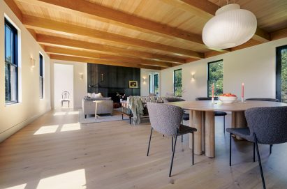 Open-plan living and dining space in Vermont house with hanging white lamp and black fireplace