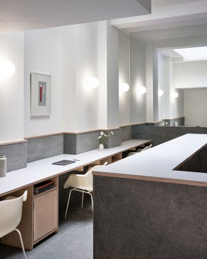 Grey carpet-lined walls in office space by Cake Architecture with white walls and off-white chairs