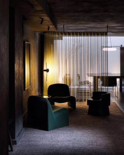 Green chairs in yellow-lit black office lounge area by Cake Architecture