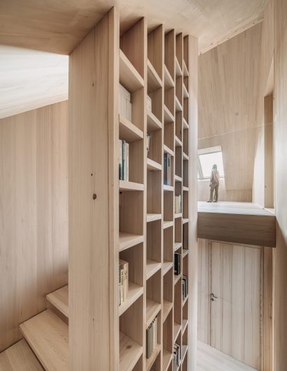 Timber storage wall along staircase in alpine house by Dunkelschwarz
