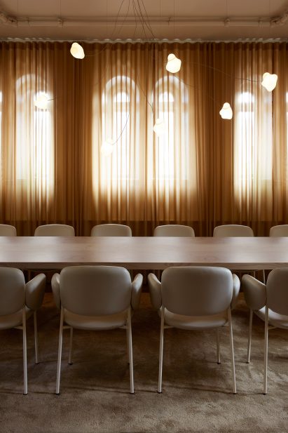 Private dining area of Stockholm restaurant by Note Design Studio with white chairs an wall of sheer-curtained windows