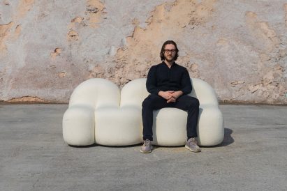 Photograph showing figure seated on white rounded sofa