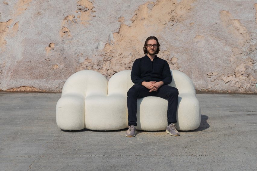 Photograph showing figure seated on white rounded sofa