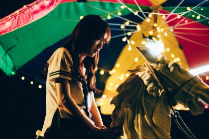 Person sitting on a horse sculpture under a colourful umbrella with fairy lights