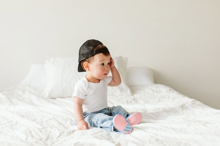A baby sitting on a bed wearing pink and blue shoes
