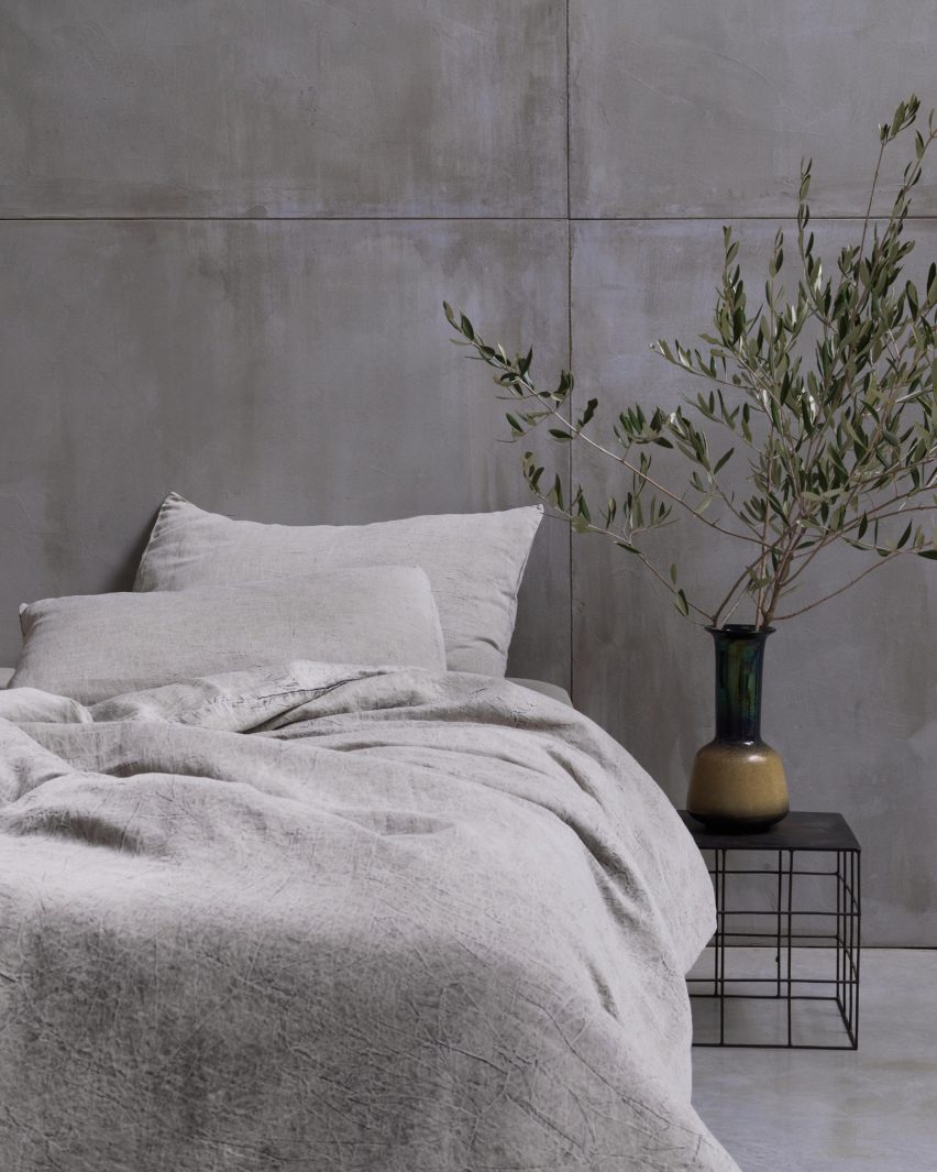 Photograph showing bed in concrete-walled bedroom with beige-coloured bedding