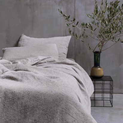 Photograph showing bed in concrete-walled bedroom with beige-coloured bedding