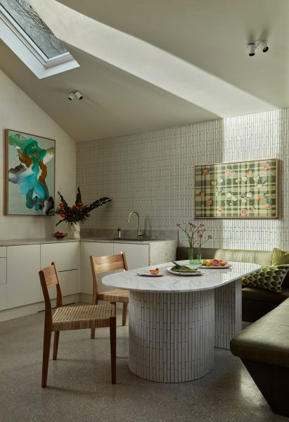 Dining area with curved white table, green seating, and skylight