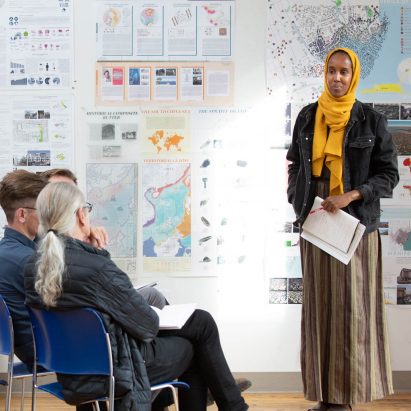 Person standing in front of an architectural presentation speaking to an audience