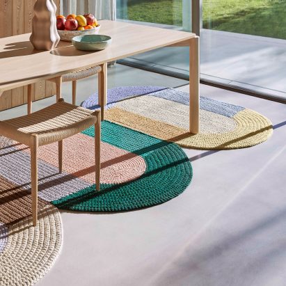 Three crochet rugs by Gan in a dining room under a wooden table and chairs