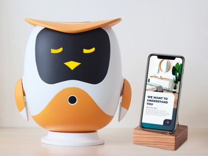 Robotic owl in black white and orange on a tabletop next to a phone by student at Hong Kong Polytechnic University