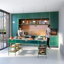 Man using Neff Slide & Hide oven while woman cuts vegetables in small green kitchen