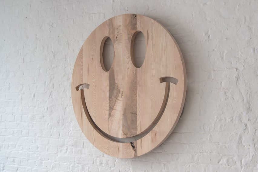 Photograph showing wooden smiley face against white-painted brick wall