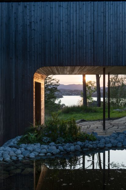 Curved two-floor timber villa on stilts over pond and patio