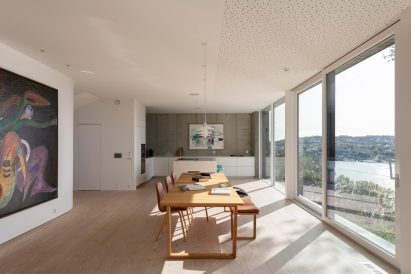 Bright minimalist kitchen, living, and dining space in Norway home with large windows showing views of lake
