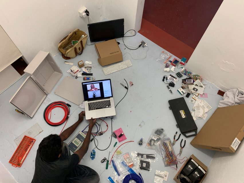 Aerial photo of a man sitting surrounded by wires and circuitry while talking to someone on an open laptop