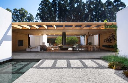 Covered living area looking onto pool and grey stone floor by Studio Guilherme Torres