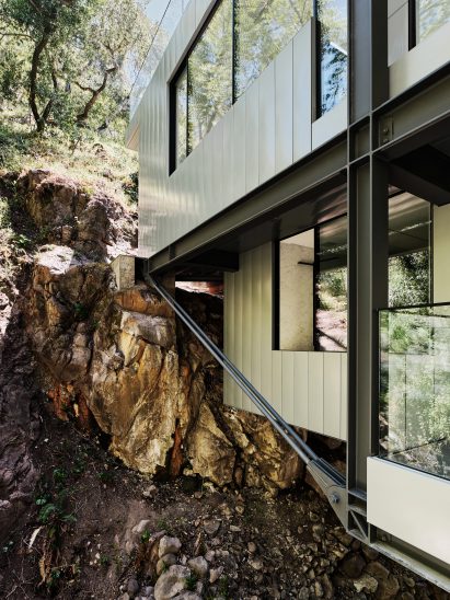 Steel structural support bars on building hovering over creek attached to side of hill