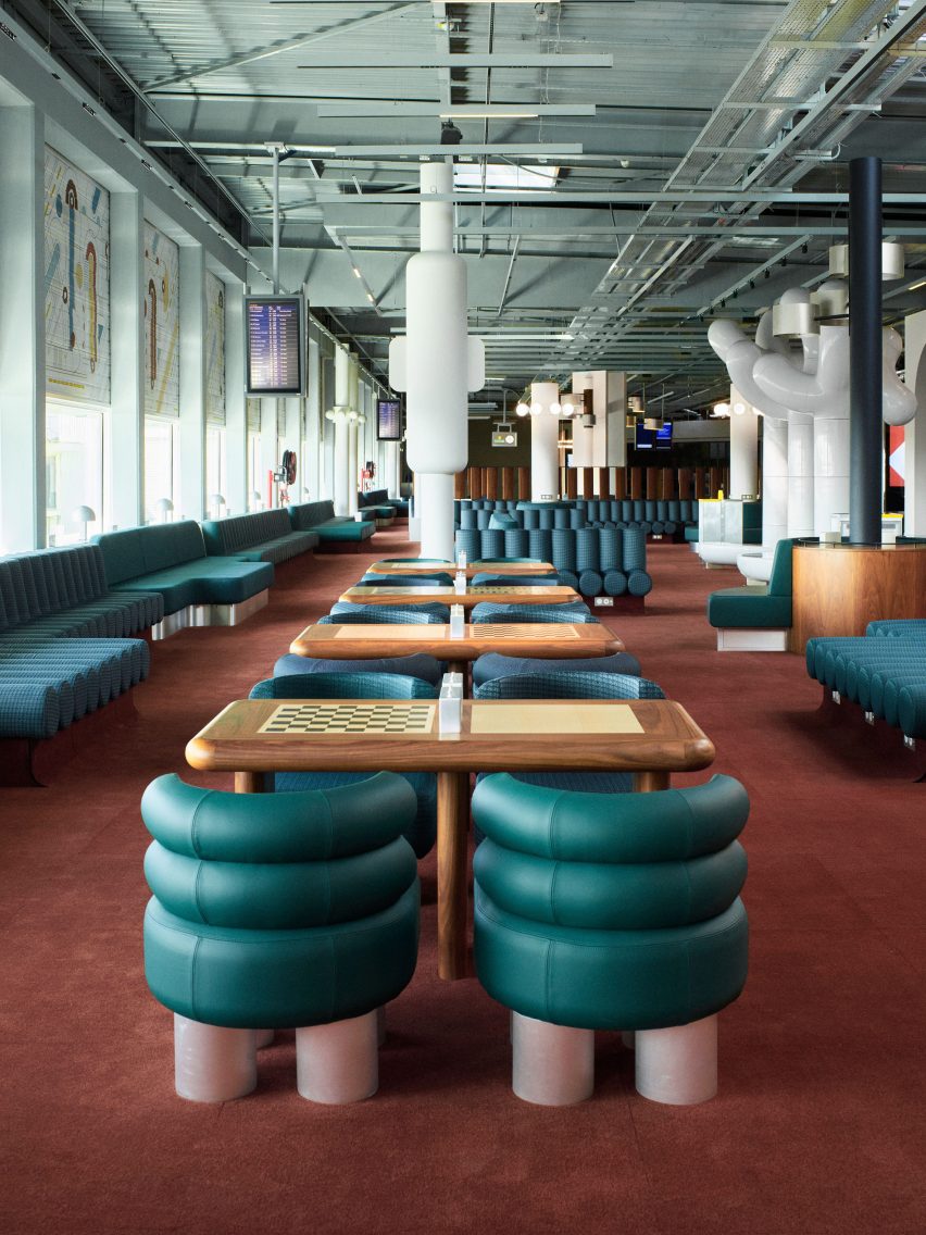 Photograph showing airport departure lounge with abstract mural above windows and green seating