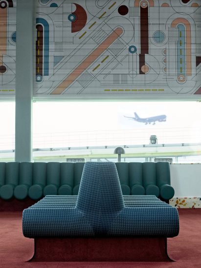 Photograph showing airport departure lounge with abstract mural above windows and green seating