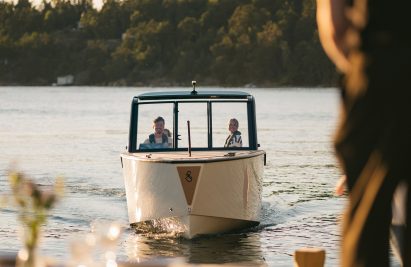 Two people sit in an X Shore 1 boat as it approaches shore