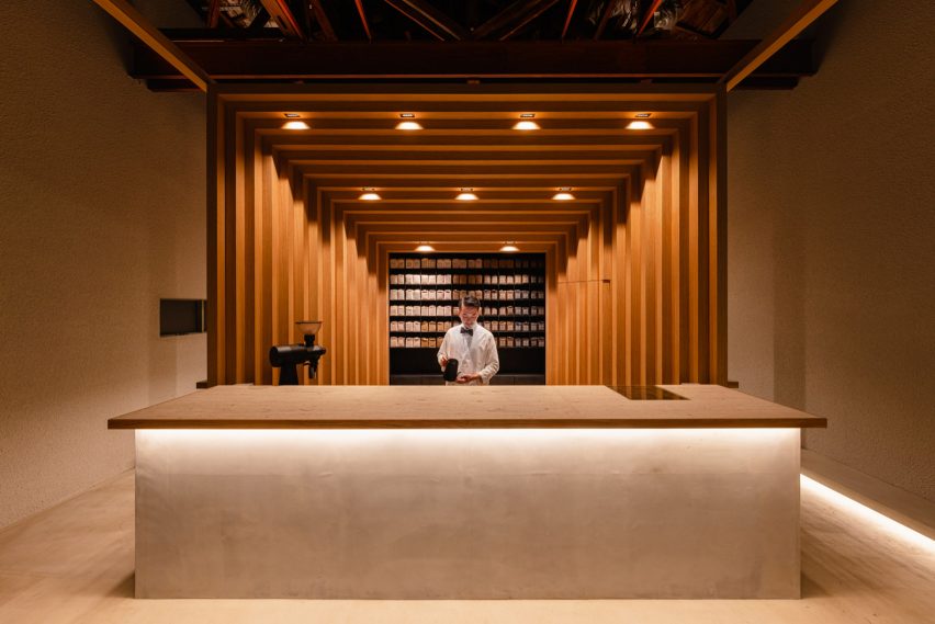 Barista behind entry counter with spotlights and wooden frame