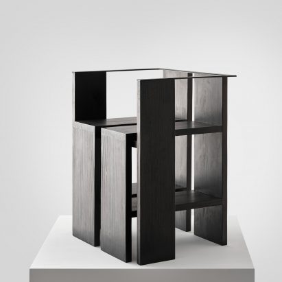 Photograph of black chair on white plinth in front of white background