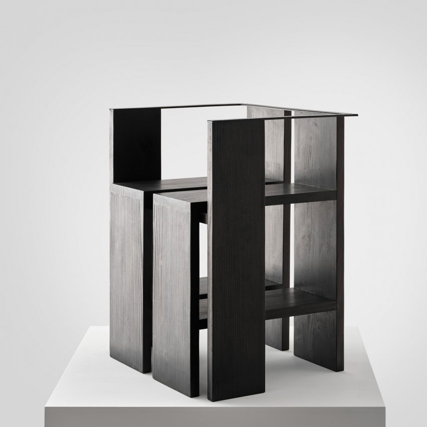 Photograph of black chair on white plinth in front of white background