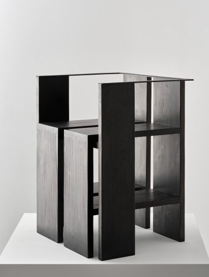 Photograph of black chair on white plinth in front of white background