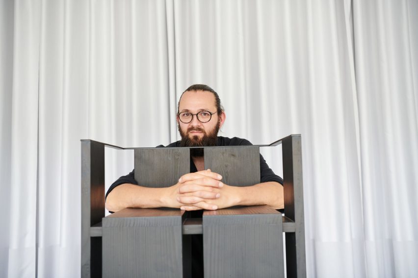 Photograph of black chair in front of white curtain with designer