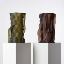 Photograph showing a green and brown-toned textural glass sculptures on white plinths