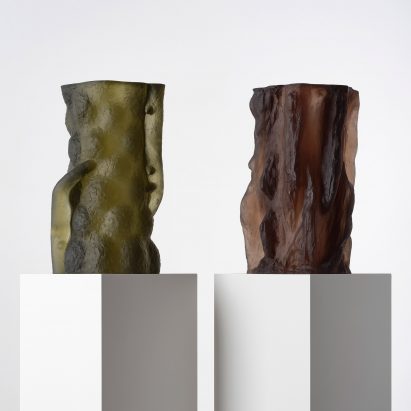 Photograph showing a green and brown-toned textural glass sculptures on white plinths