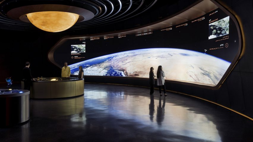 A photograph of people in a exhibition of a space station, looking towards Earth