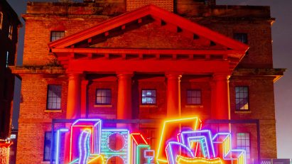 River Of Light colourful light installation by Camille Walala in front of a building at the Royal Albert Docks