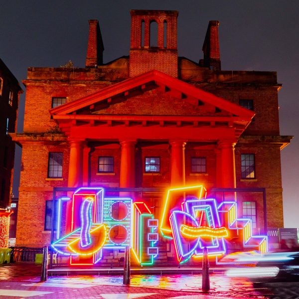 River Of Light colourful light installation by Camille Walala in front of a building at the Royal Albert Docks