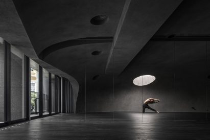 Person doing yoga in dark studio space beneath round skylight