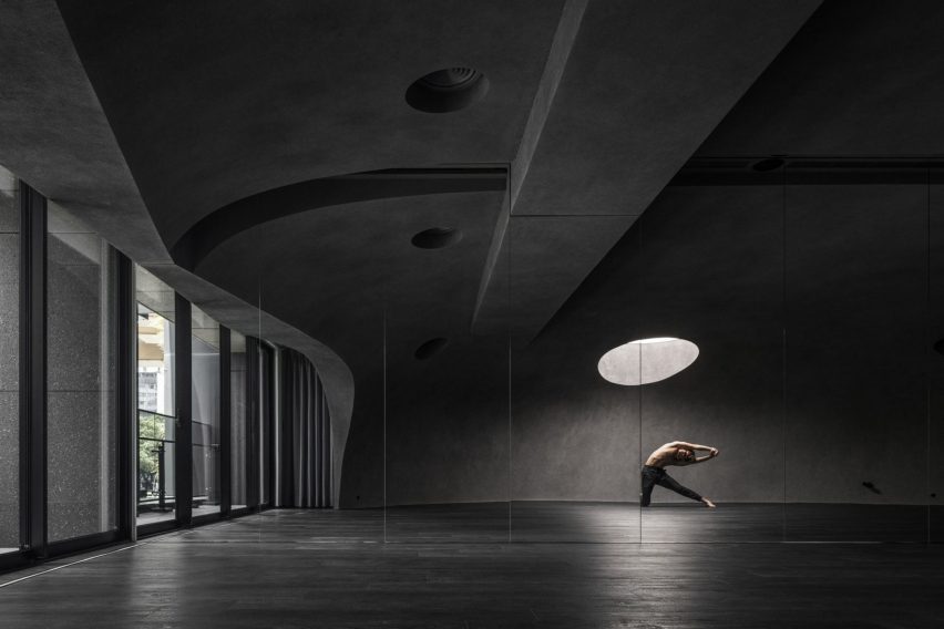 Person doing yoga in dark studio space beneath round skylight
