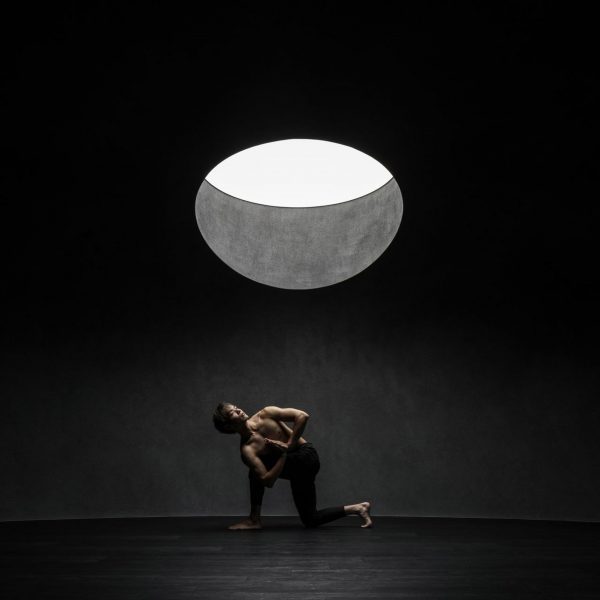Person doing yoga in dark studio space beneath round skylight
