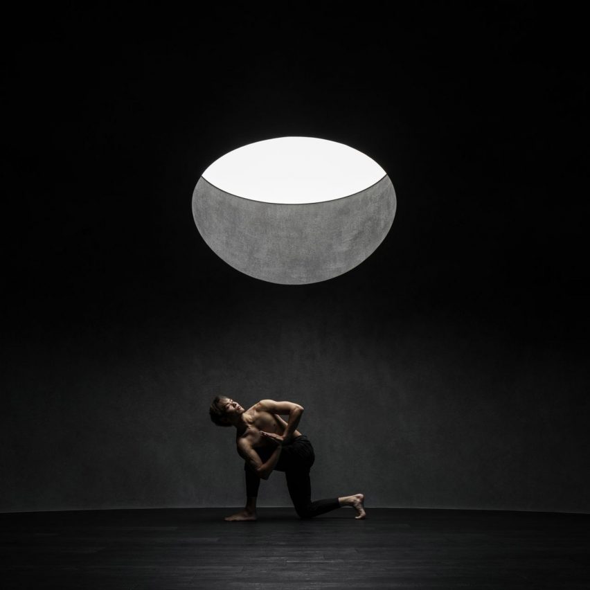 Person doing yoga in dark studio space beneath round skylight