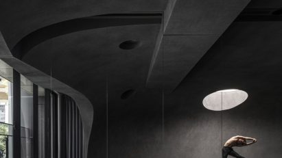 Person doing yoga in dark studio space beneath round skylight